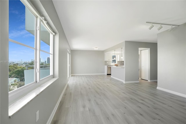 unfurnished living room with track lighting, baseboards, and light wood-type flooring