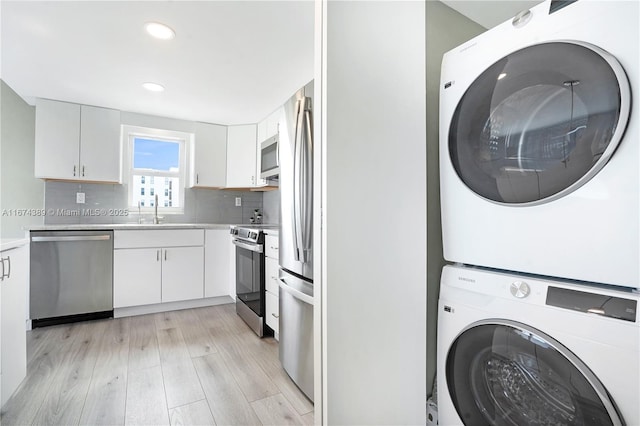 laundry area with recessed lighting, stacked washer / dryer, laundry area, a sink, and light wood-style floors
