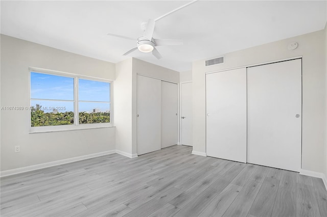 unfurnished bedroom with multiple closets, visible vents, a ceiling fan, light wood-style floors, and baseboards