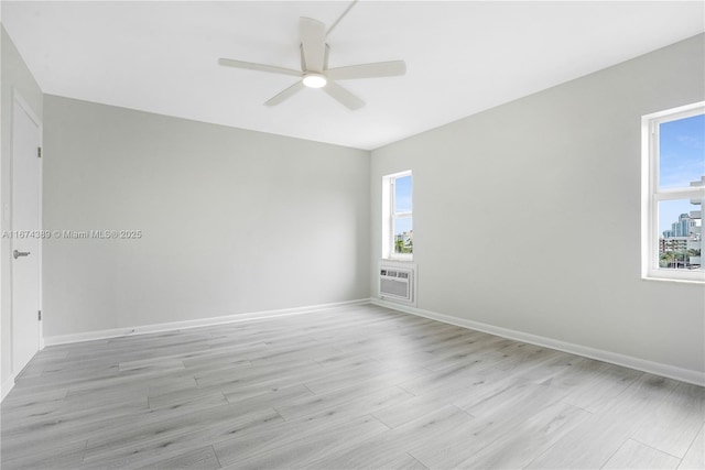empty room featuring light wood-style floors, a wall mounted air conditioner, a ceiling fan, and baseboards