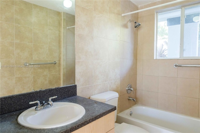 full bathroom featuring toilet, tiled shower / bath, vanity, and tile walls