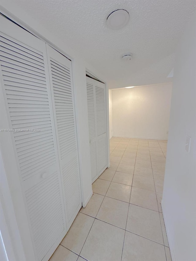 hallway with a textured ceiling and light tile patterned floors