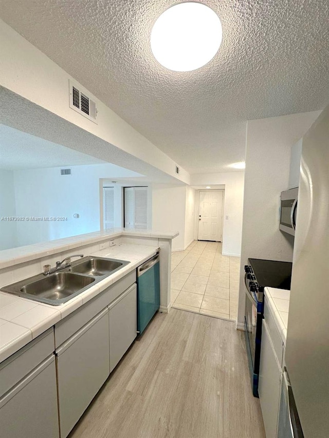 kitchen featuring sink, light hardwood / wood-style floors, appliances with stainless steel finishes, tile countertops, and a textured ceiling