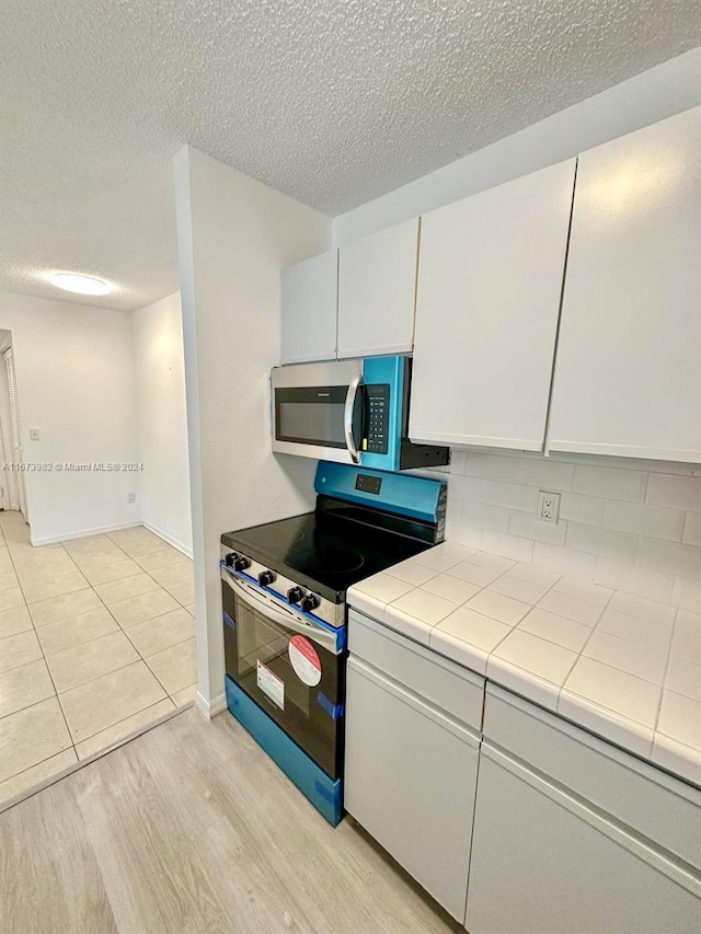 kitchen with light wood-type flooring, white cabinetry, tile countertops, electric stove, and a textured ceiling