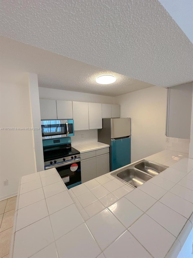 4045 W Mcnab Rd Unit 106G, Pompano Beach, FL 33069 - kitchen with stainless steel appliances, a sink, a textured ceiling, tile counters, and light tile patterned floors