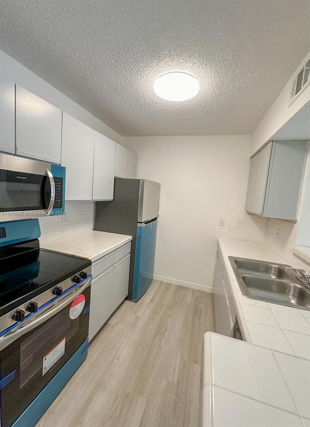 kitchen featuring white cabinets, sink, a textured ceiling, appliances with stainless steel finishes, and light wood-type flooring