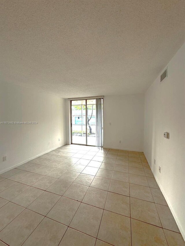 4045 W Mcnab Rd Unit 106G, Pompano Beach, FL 33069 - spare room featuring a textured ceiling, light tile patterned floors, a wall of windows, and baseboards