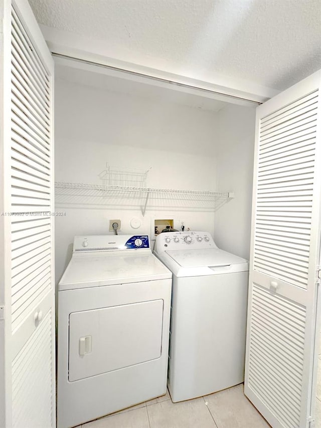 washroom with independent washer and dryer, light tile patterned floors, and a textured ceiling