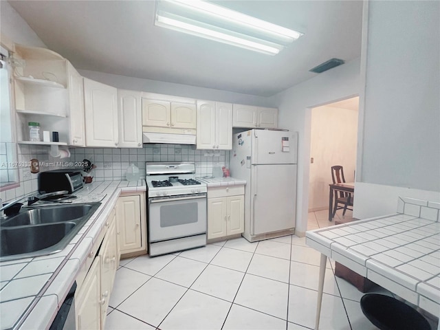 kitchen featuring light tile patterned floors, tile counters, backsplash, white appliances, and sink