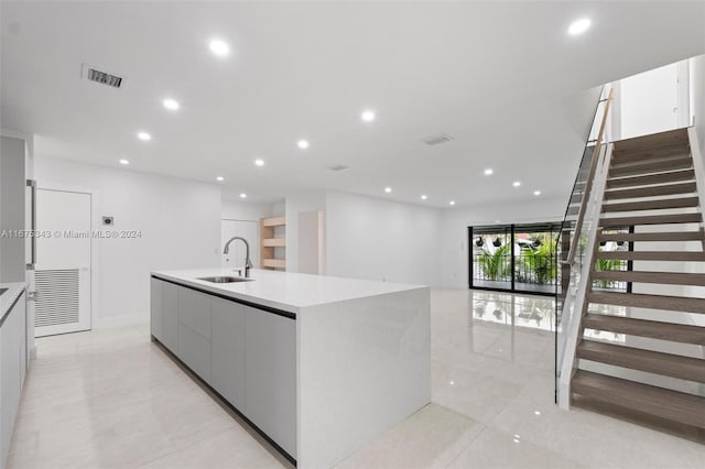 kitchen with light tile patterned floors, a large island with sink, sink, and white cabinetry