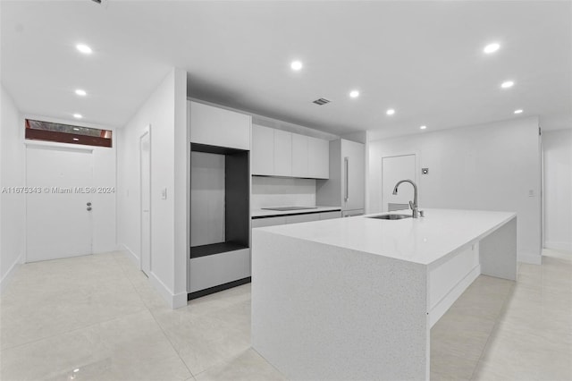 kitchen with black electric cooktop, white cabinets, a kitchen island with sink, and sink