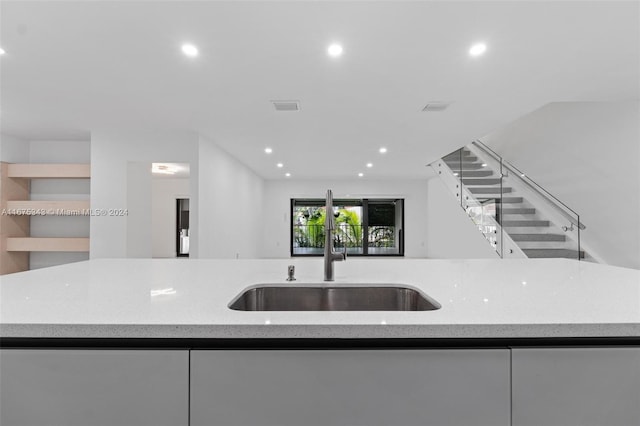 kitchen featuring a center island with sink, light stone counters, sink, and white cabinets