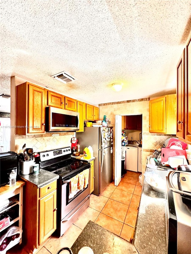 kitchen featuring a textured ceiling, range with electric stovetop, washing machine and clothes dryer, and light tile patterned flooring