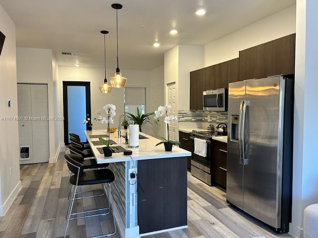 kitchen with a breakfast bar area, appliances with stainless steel finishes, hanging light fixtures, and light hardwood / wood-style floors