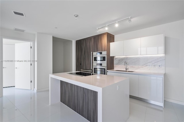 kitchen with stainless steel double oven, black electric cooktop, an island with sink, sink, and white cabinetry