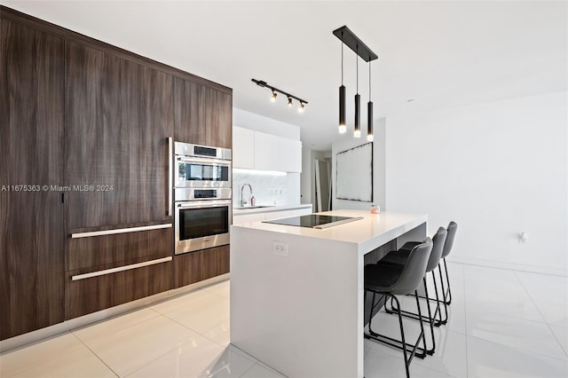 kitchen featuring double oven, hanging light fixtures, a center island with sink, a kitchen bar, and white cabinetry