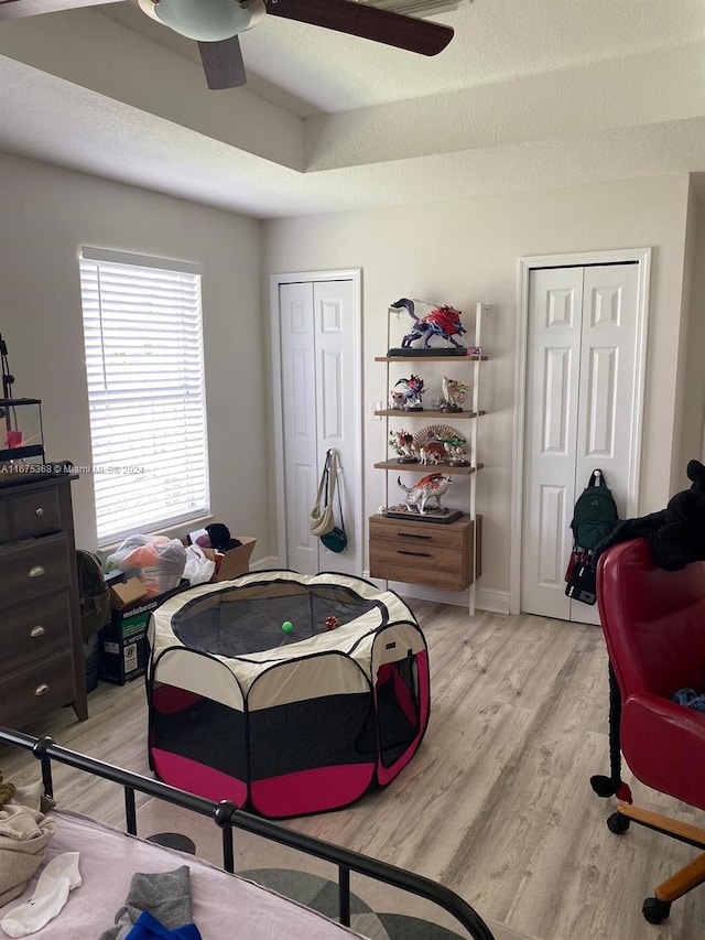 bedroom featuring two closets, light hardwood / wood-style floors, a textured ceiling, and ceiling fan