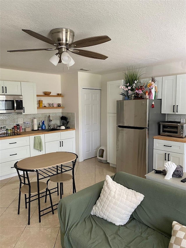 kitchen with appliances with stainless steel finishes, ceiling fan, light tile patterned floors, and white cabinets