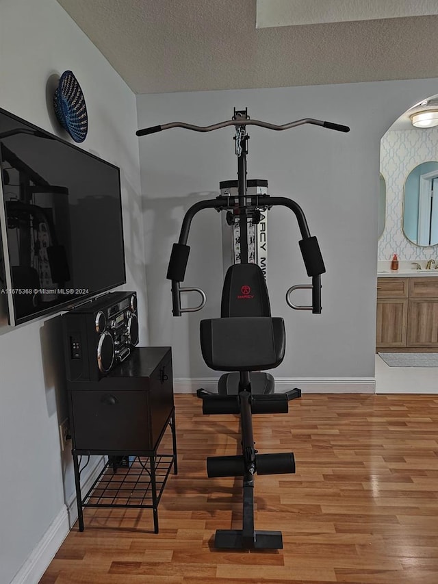 exercise room featuring light wood-type flooring, sink, and a textured ceiling