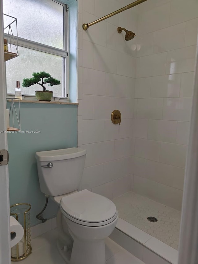 bathroom with a tile shower, toilet, and tile patterned floors