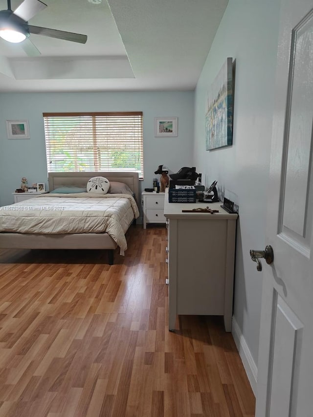 bedroom with ceiling fan, a tray ceiling, and hardwood / wood-style floors