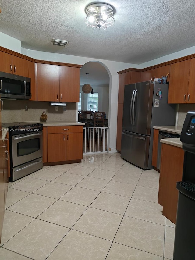 kitchen featuring light tile patterned flooring, pendant lighting, appliances with stainless steel finishes, and a textured ceiling