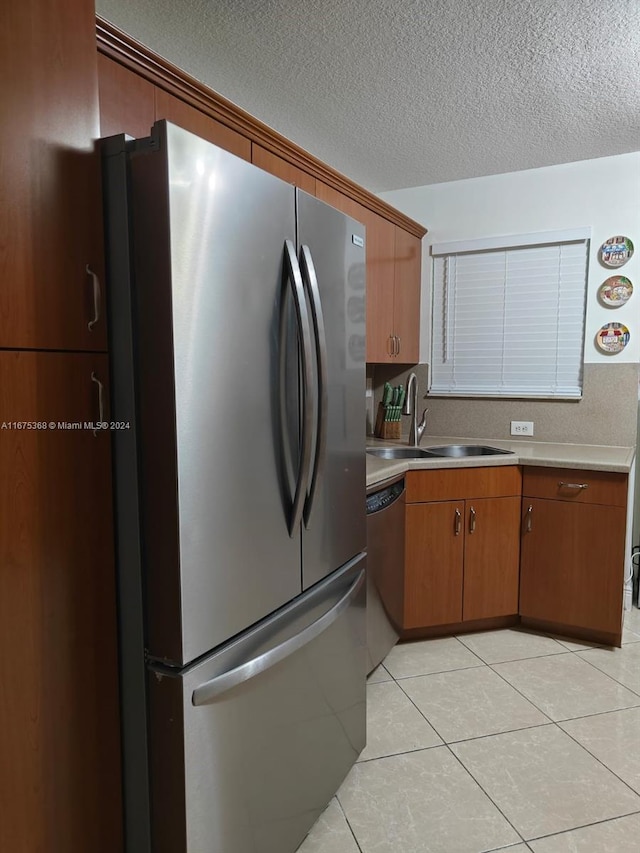 kitchen featuring appliances with stainless steel finishes, sink, light tile patterned floors, and a textured ceiling