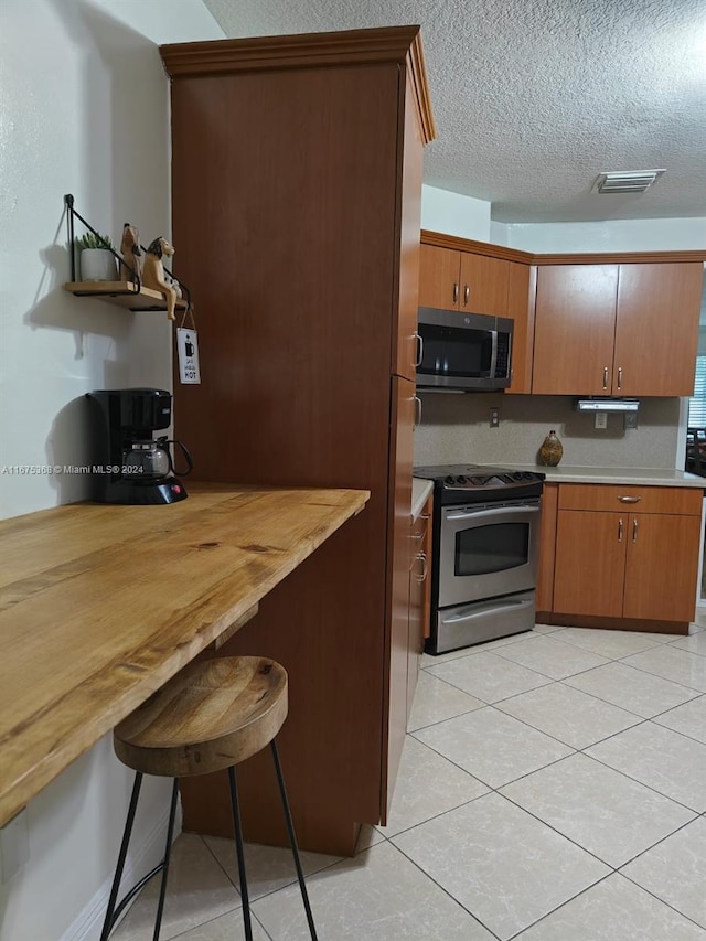 kitchen featuring stainless steel appliances, wooden counters, a kitchen bar, light tile patterned floors, and a textured ceiling