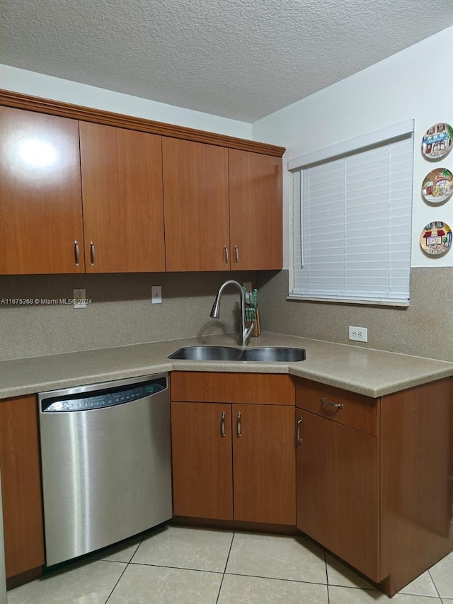 kitchen featuring sink, stainless steel dishwasher, light tile patterned floors, and a textured ceiling