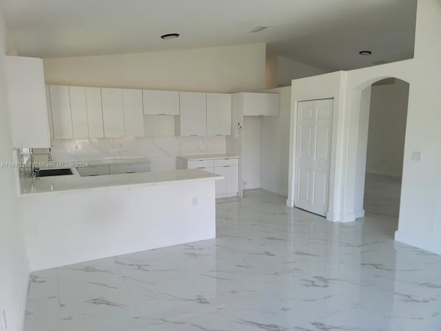 kitchen featuring white cabinets, sink, kitchen peninsula, vaulted ceiling, and decorative backsplash