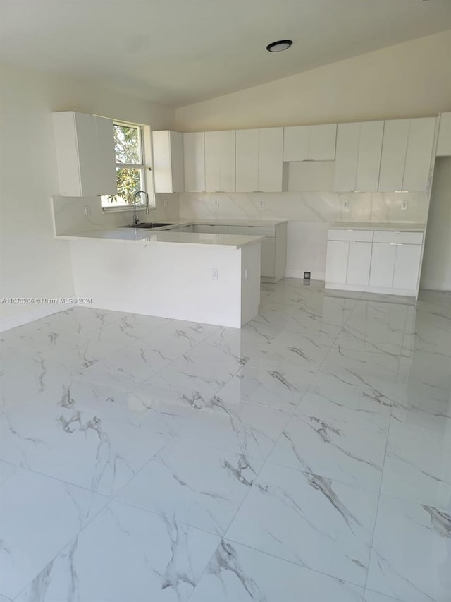 kitchen with lofted ceiling, decorative backsplash, white cabinets, sink, and kitchen peninsula