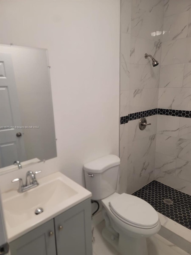 bathroom with a tile shower, vanity, and toilet