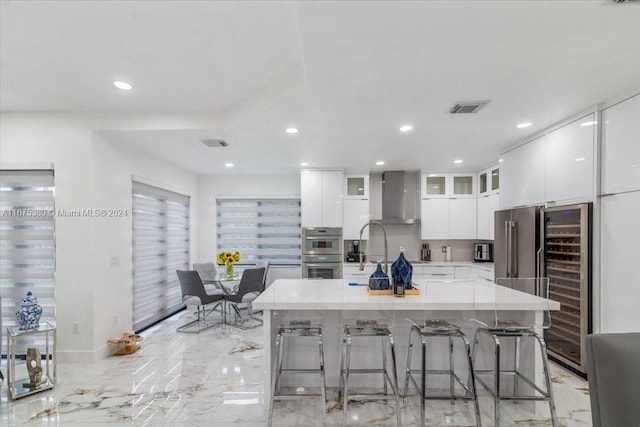 kitchen with wall chimney range hood, white cabinets, a breakfast bar, and a large island