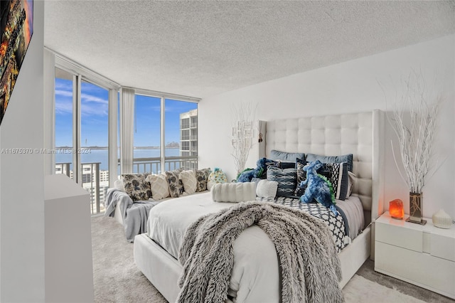 bedroom with a water view, light colored carpet, floor to ceiling windows, and a textured ceiling