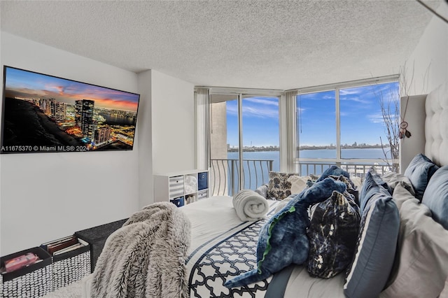 bedroom with a water view, a wall of windows, and a textured ceiling