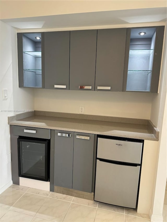 bar featuring beverage cooler, light tile patterned floors, and gray cabinetry