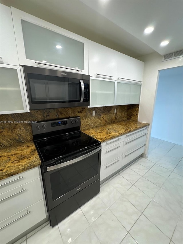 kitchen featuring light tile patterned flooring, dark stone counters, white cabinetry, black range with electric cooktop, and backsplash