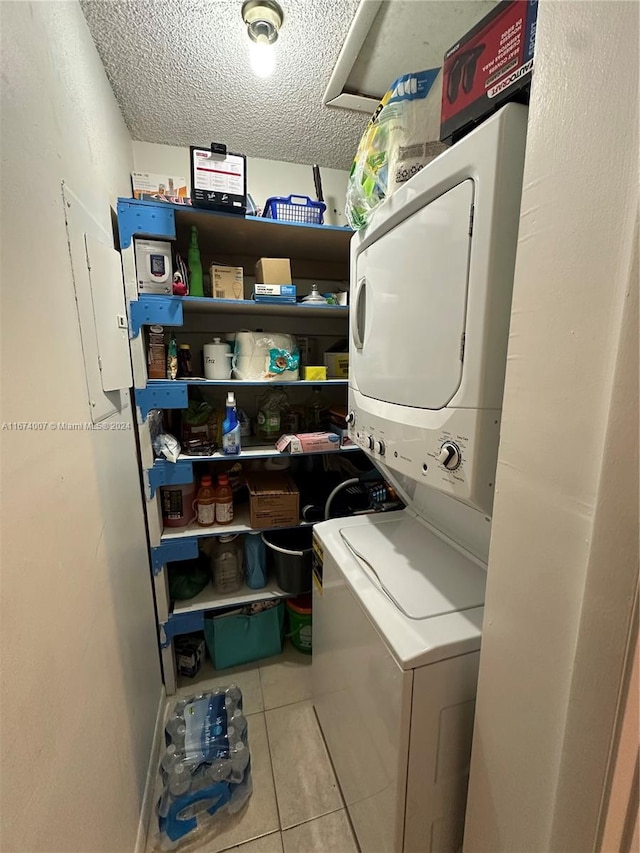 laundry room featuring stacked washer / dryer, light tile patterned floors, and a textured ceiling