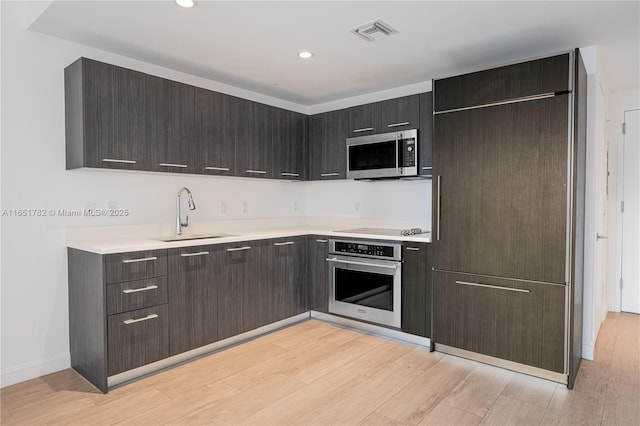 kitchen featuring dark brown cabinetry, appliances with stainless steel finishes, sink, and light hardwood / wood-style flooring