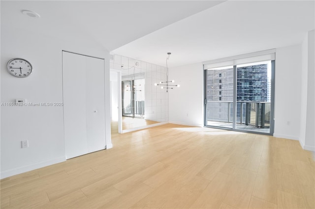 empty room featuring a notable chandelier, floor to ceiling windows, and light wood-type flooring