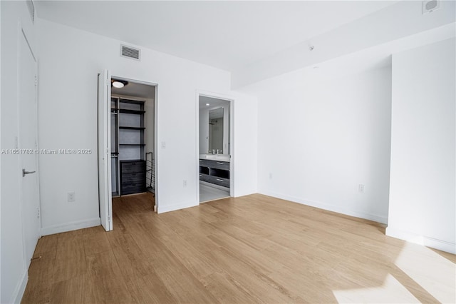 unfurnished bedroom featuring ensuite bathroom, a spacious closet, a closet, and light wood-type flooring