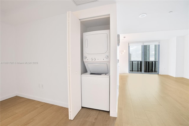 laundry area with stacked washer and dryer and light hardwood / wood-style flooring