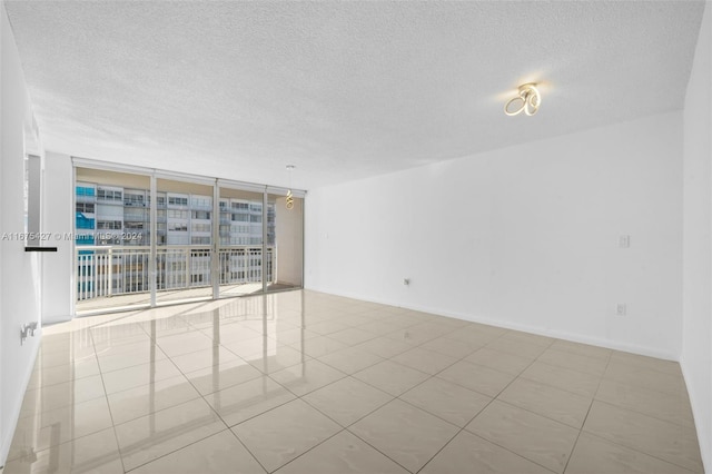 empty room with a textured ceiling, floor to ceiling windows, and light tile patterned flooring