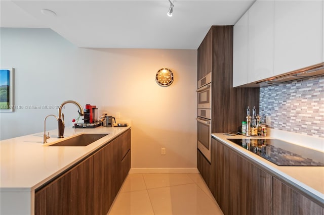 kitchen with decorative backsplash, white cabinets, black electric stovetop, sink, and light tile patterned floors