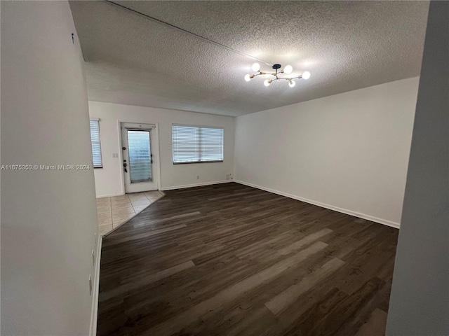 unfurnished room with a textured ceiling, a notable chandelier, and dark hardwood / wood-style floors