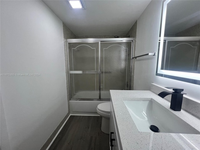 full bathroom with vanity, toilet, wood-type flooring, and enclosed tub / shower combo