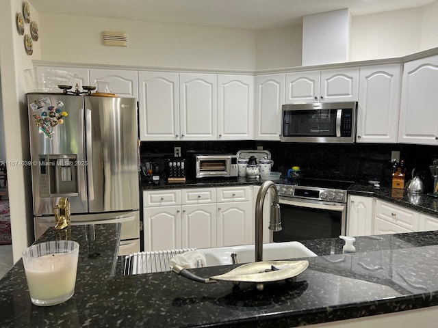 kitchen featuring stainless steel appliances, white cabinetry, tasteful backsplash, and dark stone countertops