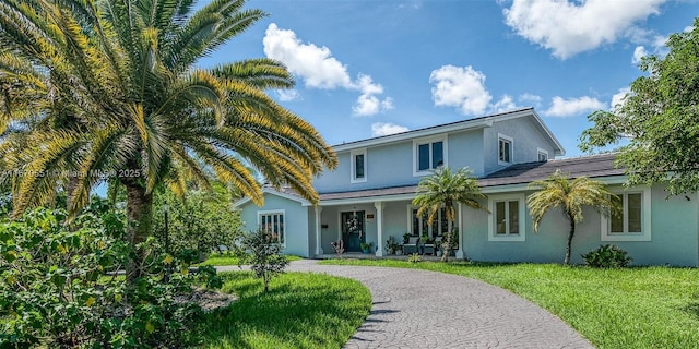 traditional home with driveway, a front lawn, a porch, and stucco siding