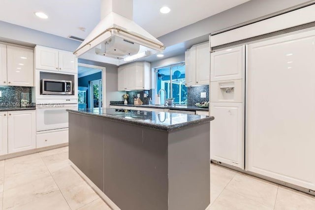 kitchen with white cabinetry, a center island, white oven, tasteful backsplash, and dark stone counters