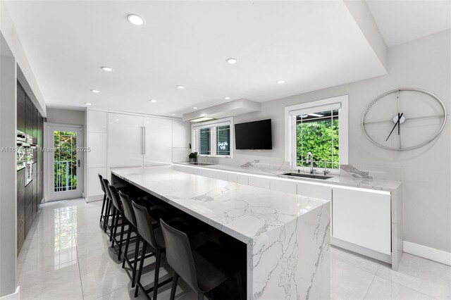 kitchen featuring a kitchen bar, sink, light stone counters, a kitchen island, and white cabinets